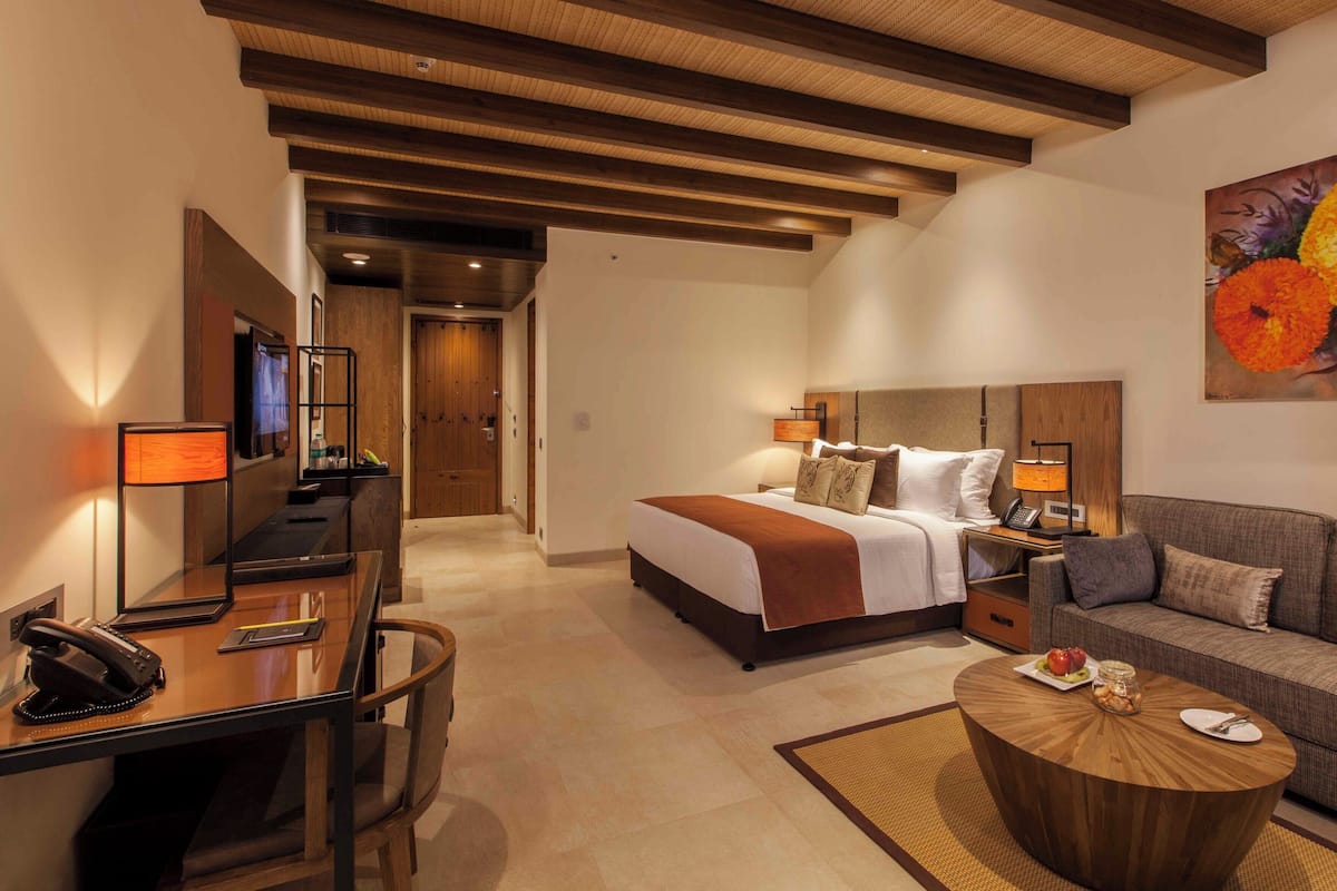 A hotel room with a bed, a desk with a telephone, a sofa, and a painting of flowers on the wall.