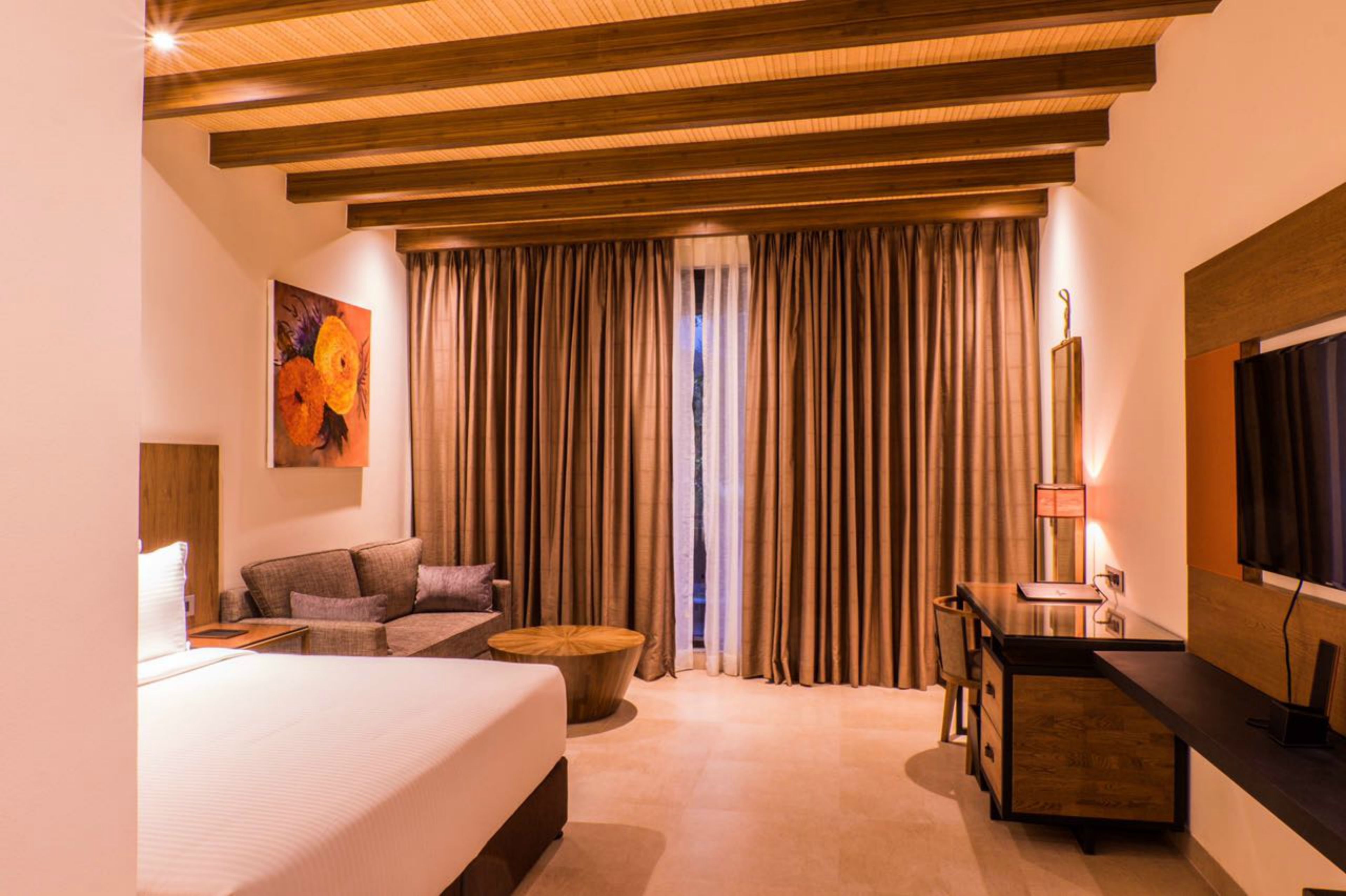 A hotel room with a bed, a sofa, a desk, and a large window with curtains.
