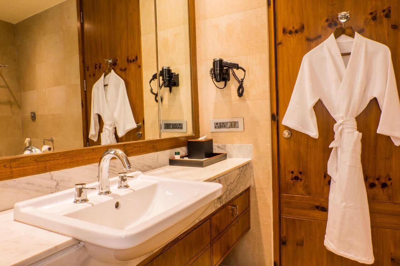 A bathroom with a large mirror, a white sink, a hairdryer, and a robe hanging on the wall.