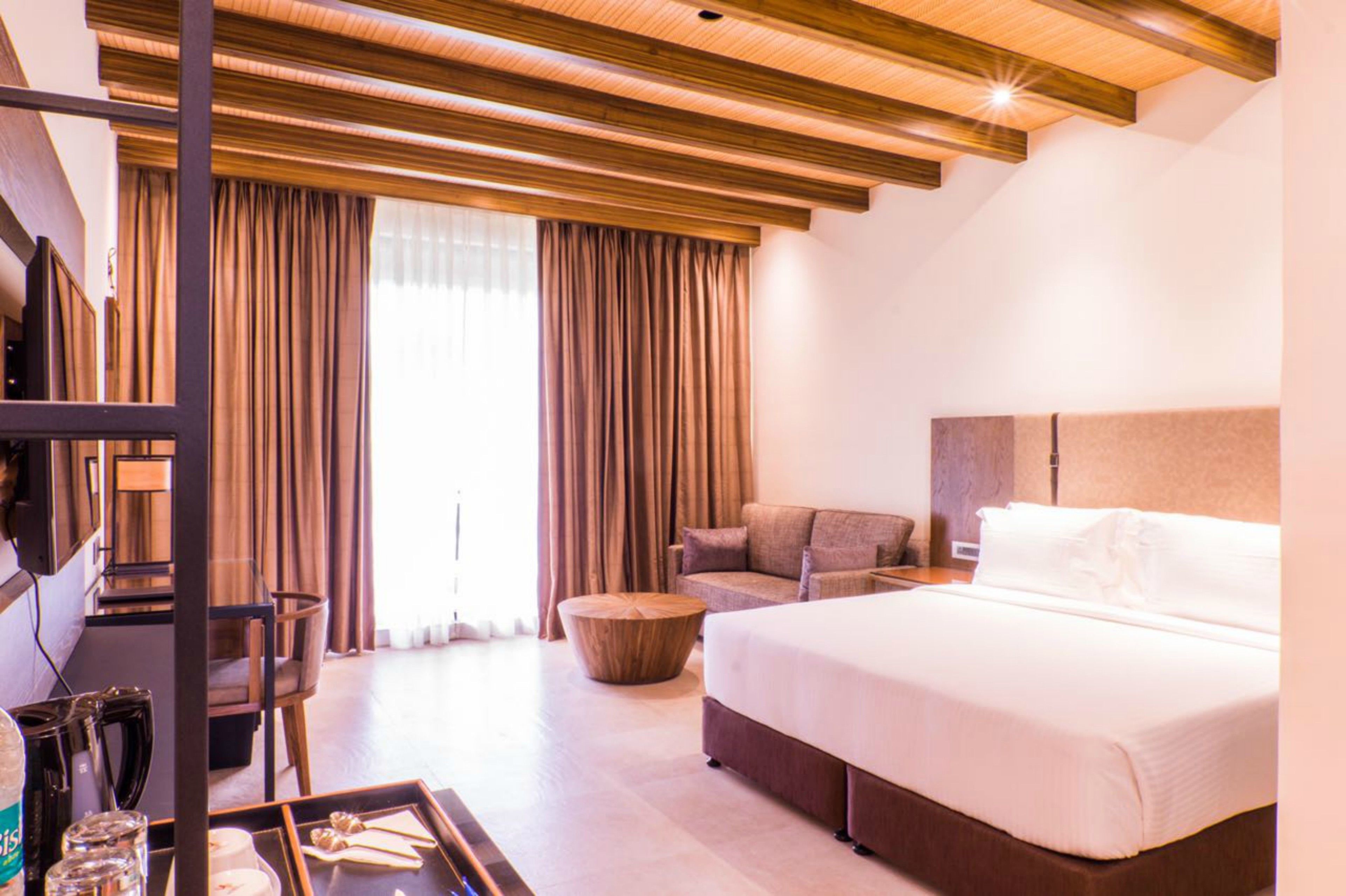 A hotel room with a large bed, a sofa, a desk with a computer, and a TV.