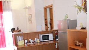A compact kitchen with a microwave, refrigerator, and a small dining area with chairs and a table. - Copenaghen House (Sassari)