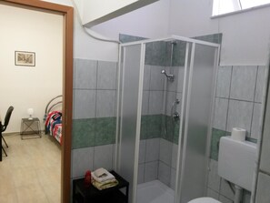 A bathroom with a shower, toilet, and a small table with towels.