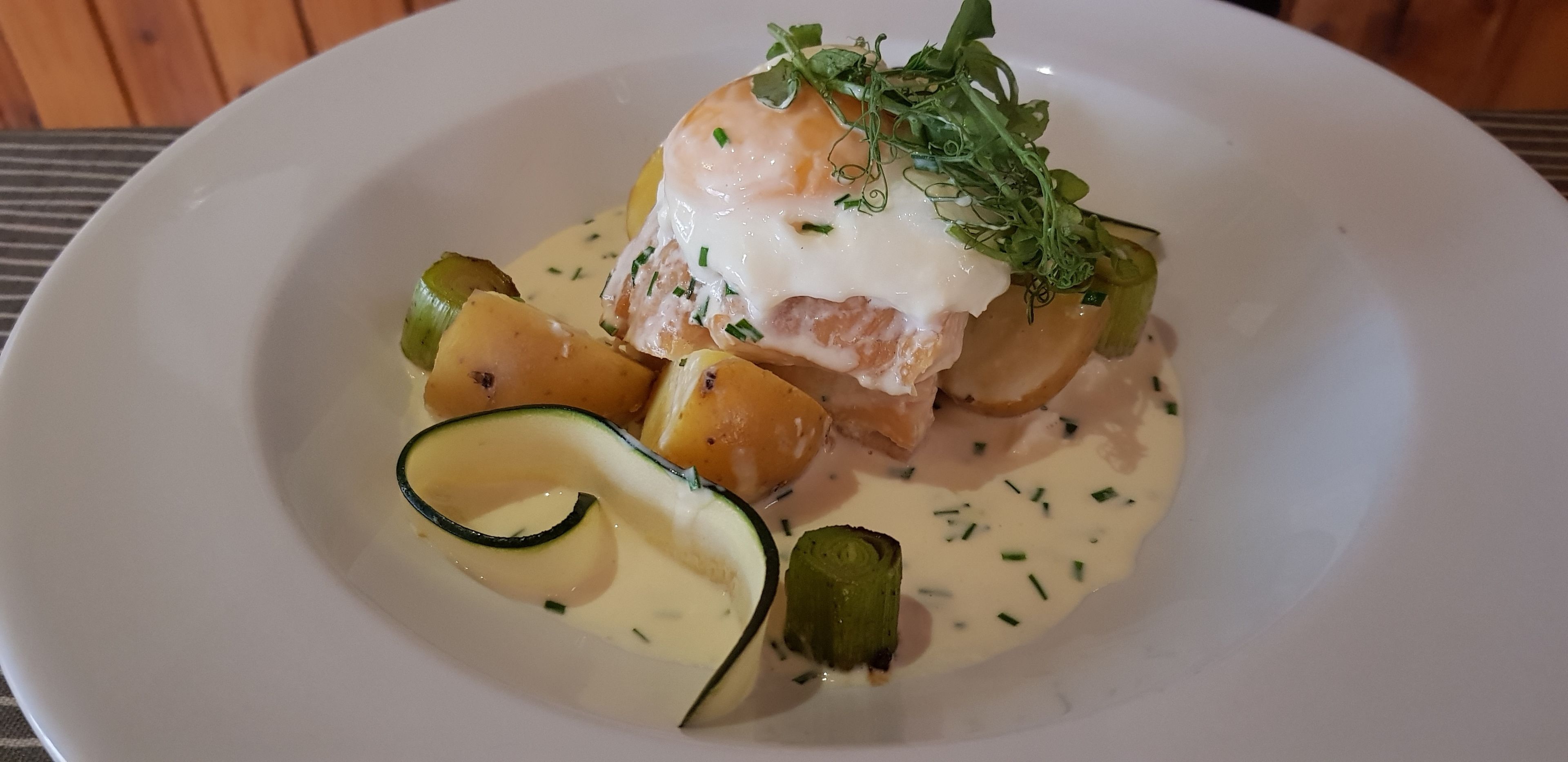 A plate of food with poached eggs, potatoes, and zucchini.