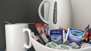 A white coffee maker, a white mug, and a bowl containing various coffee packets and a Tetley tea box.