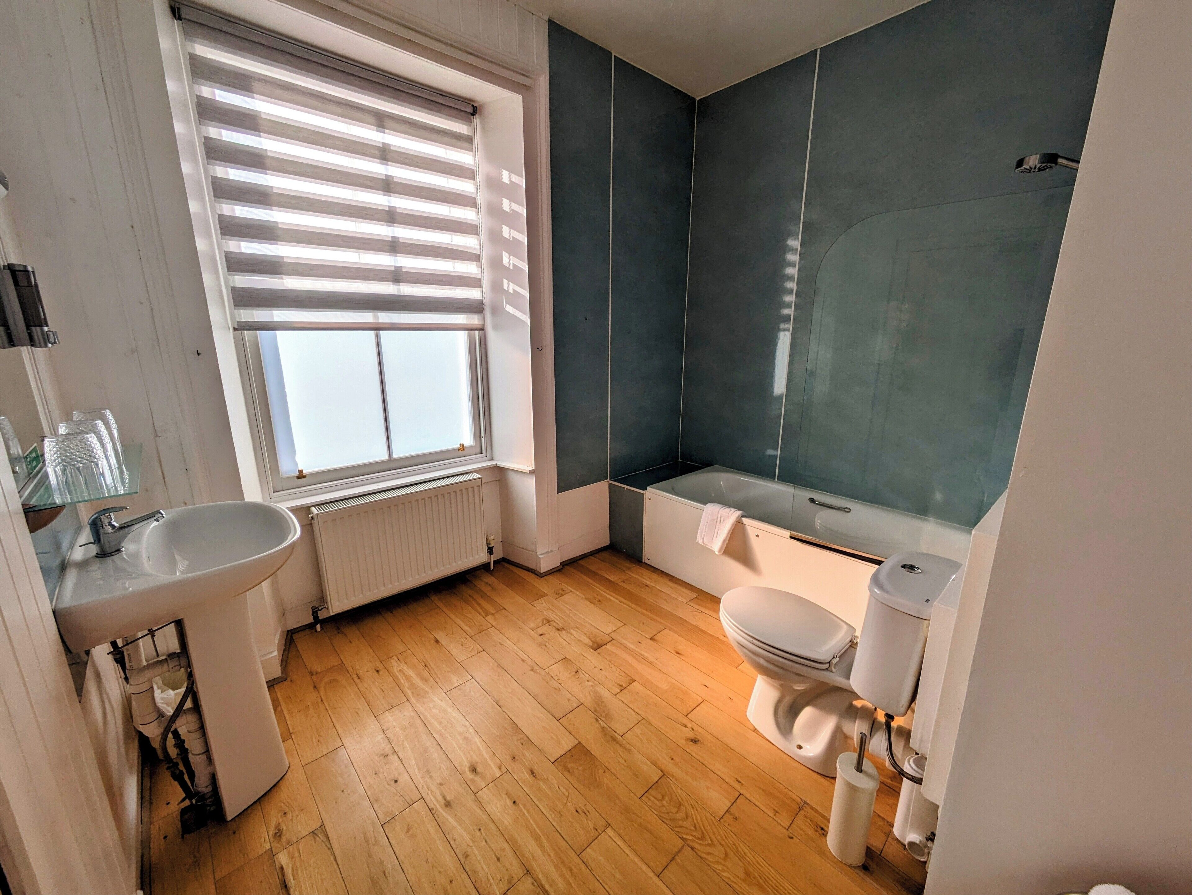 A modern bathroom with a wooden floor, a white sink, a toilet, and a bathtub.