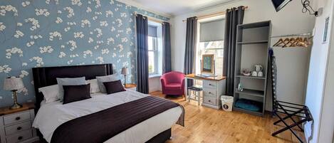 A bedroom with a bed, a desk, a chair, a TV, and a wardrobe.