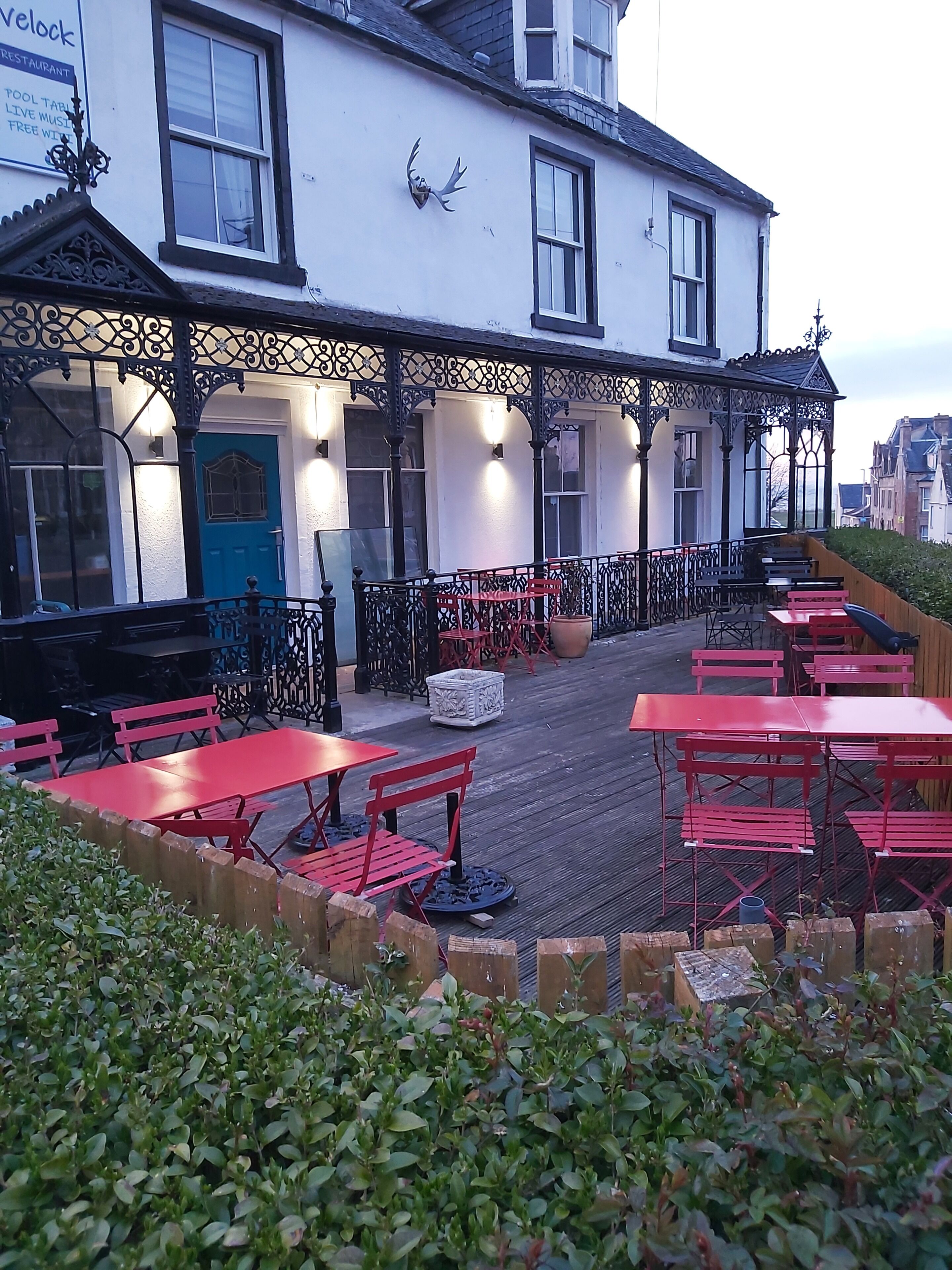 A building with a terrace featuring red tables and benches, a blue door, and a decorative antler mounted on the wall.