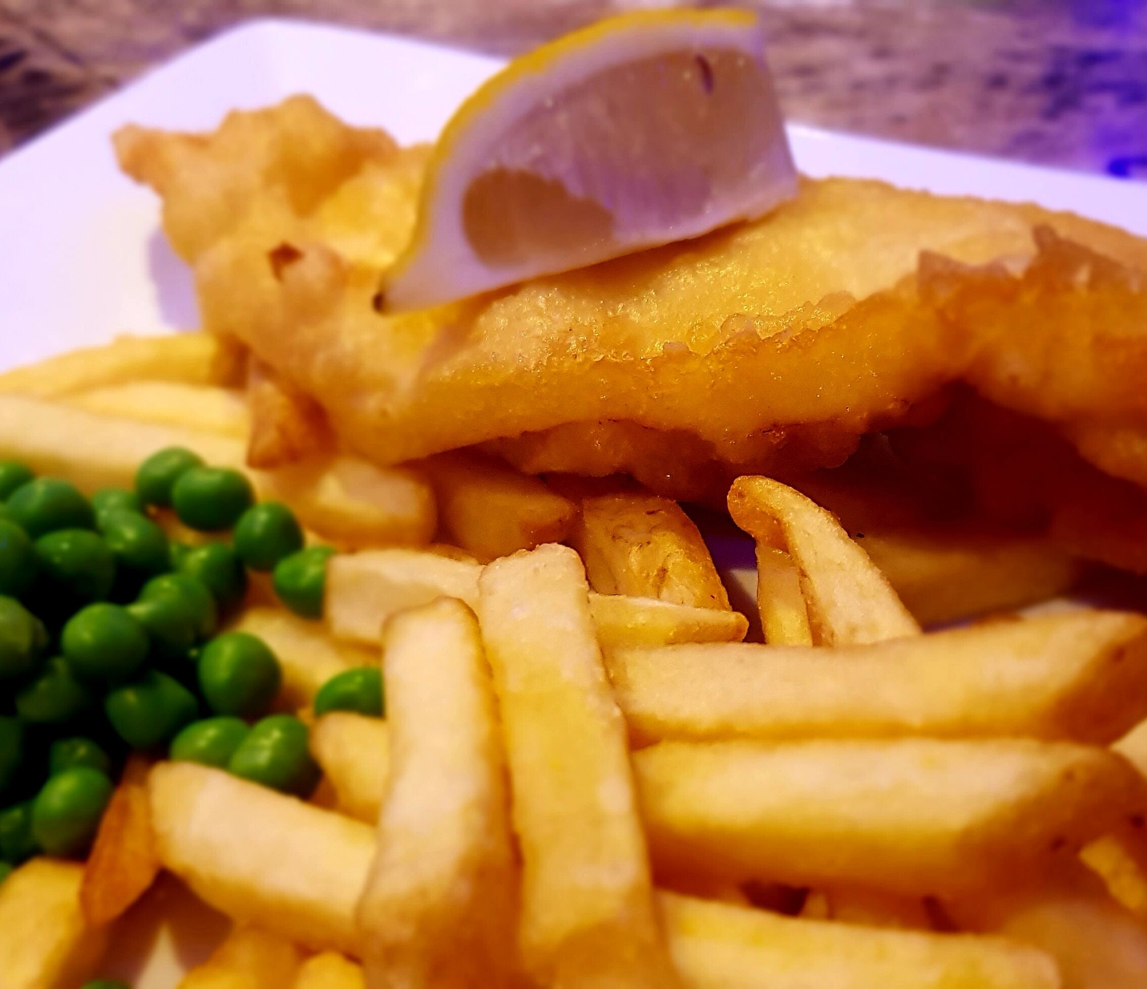 A plate of fish and chips with peas and a lemon wedge.