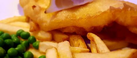 A plate of fish and chips with peas and a lemon wedge.