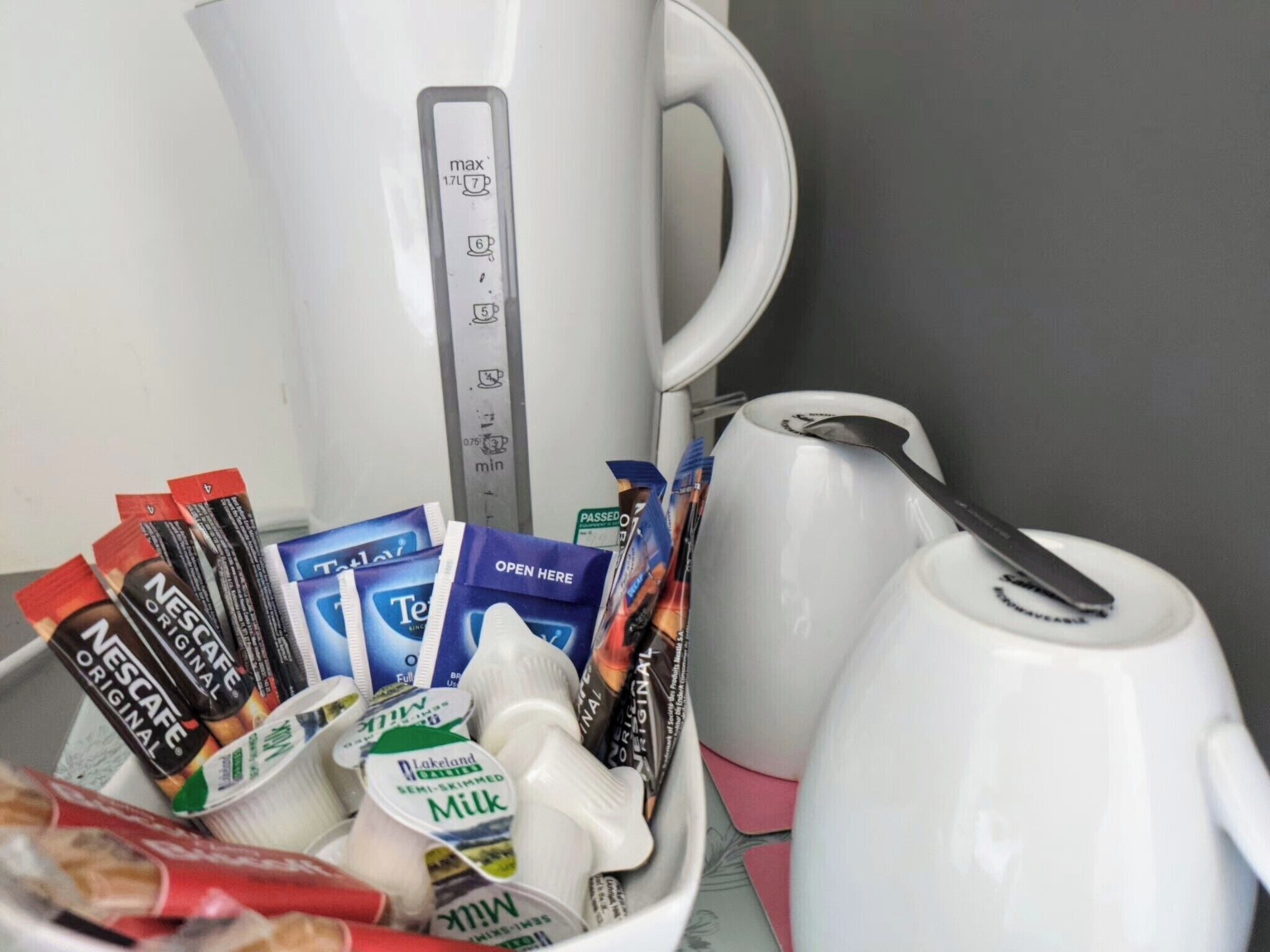 A coffee maker, a mug, and a bowl containing various coffee pods and milk cartons.