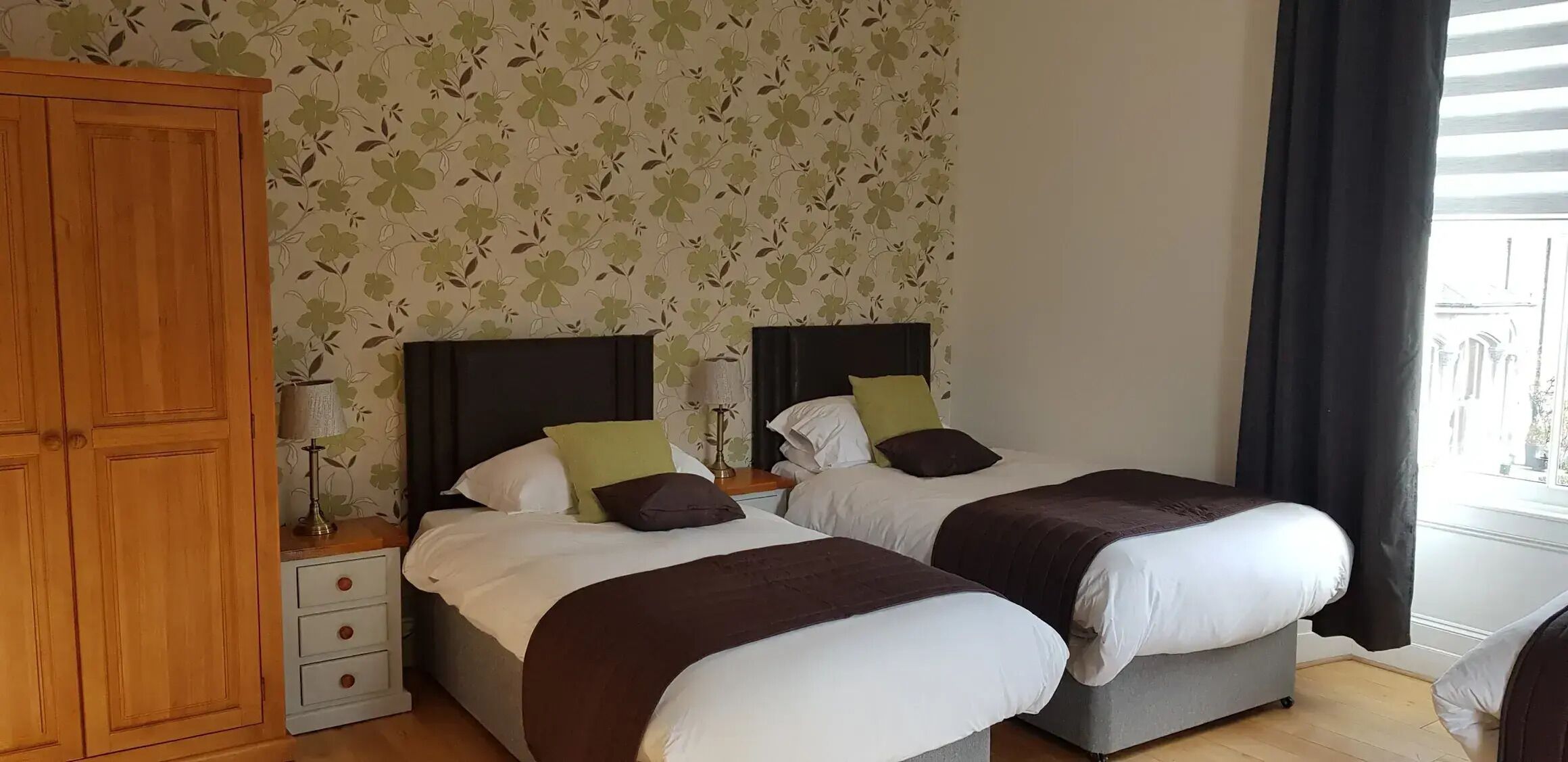 A hotel room with two beds, a wardrobe, and a window with curtains.