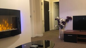 Uma sala de estar moderna com televisão de tela plana na parede, mesa de centro de vidro, lareira com revestimento de pedra e sofá com tapete estampado.