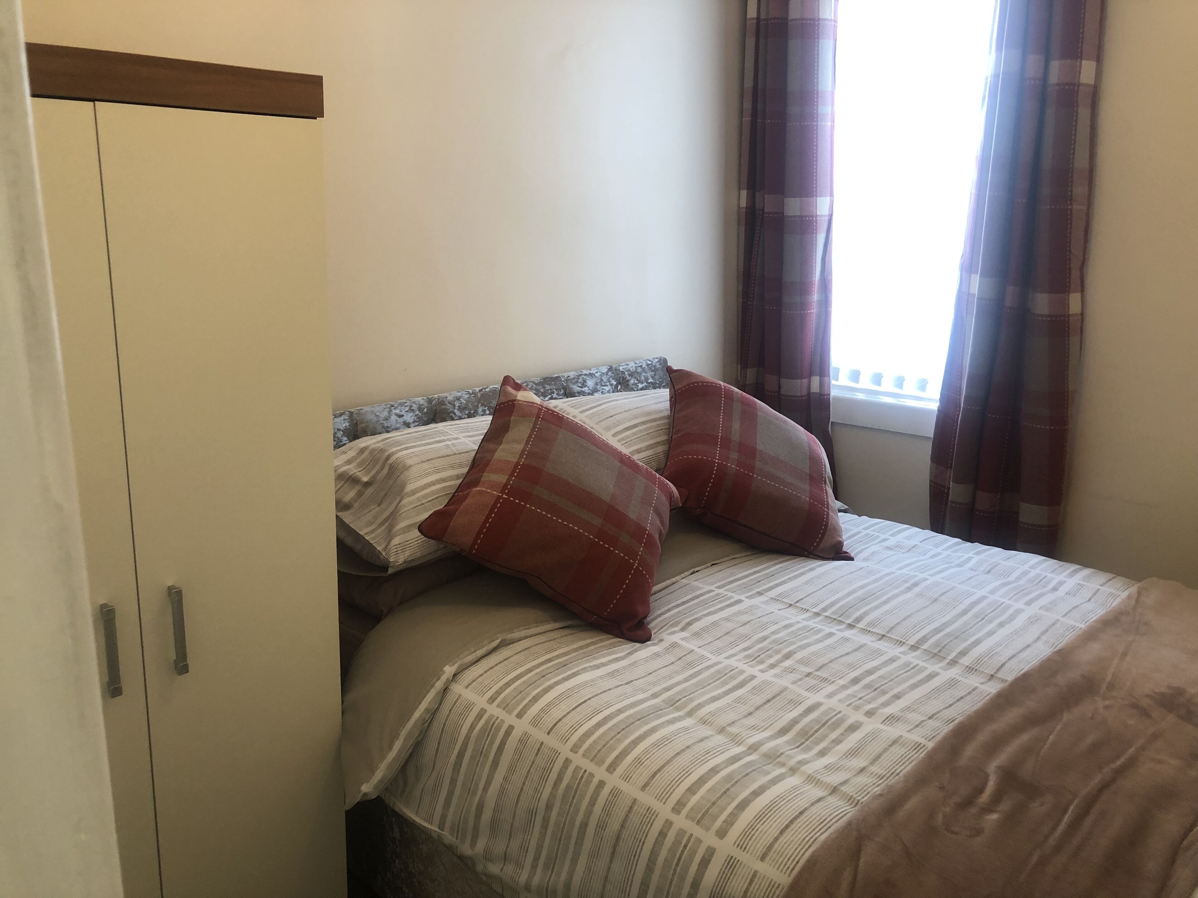 A bedroom with a bed, two pillows, a window with curtains, and a wardrobe.
