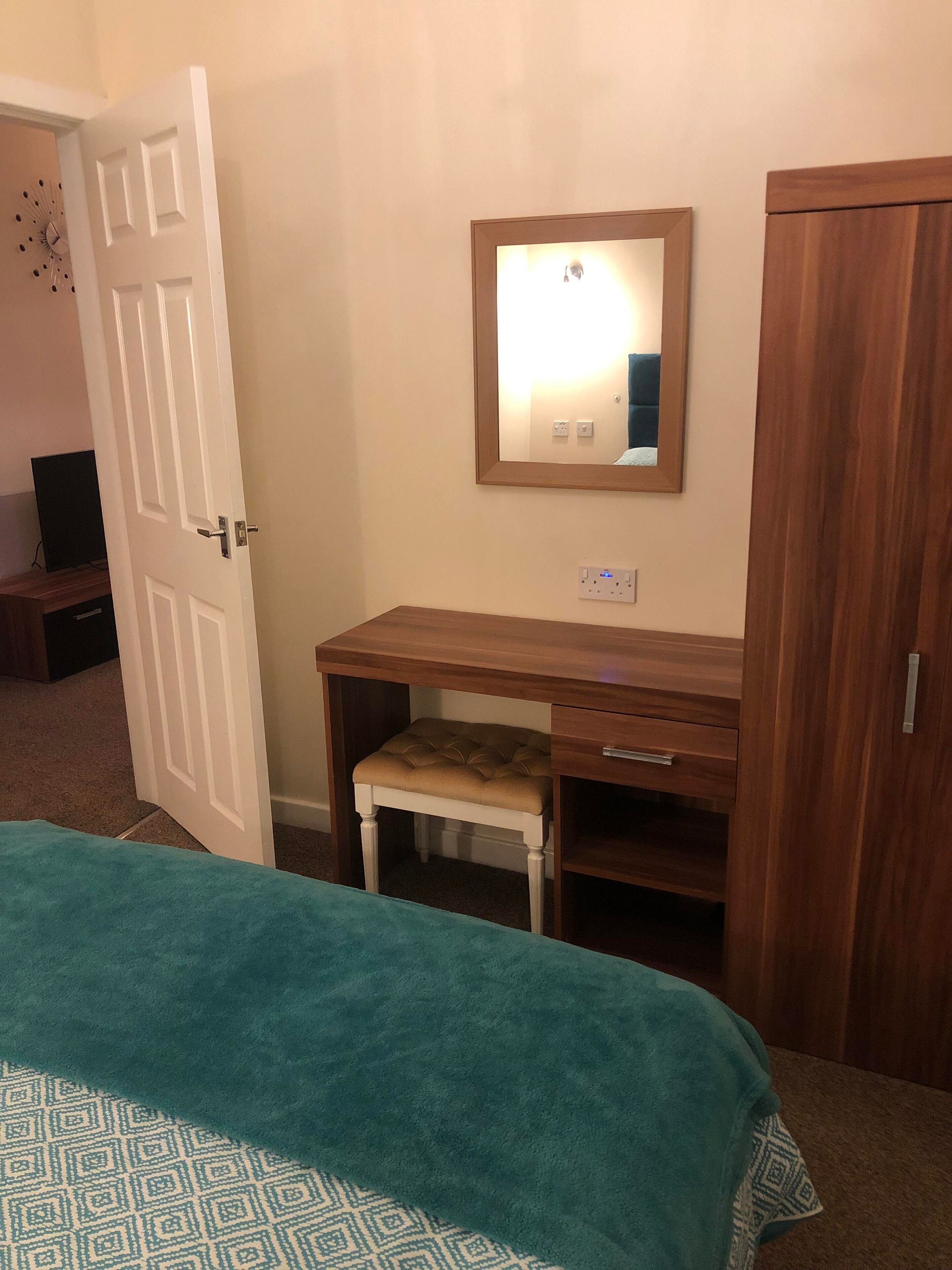 A bedroom with a bed, a wooden desk with a chair, a mirror, and a wardrobe.