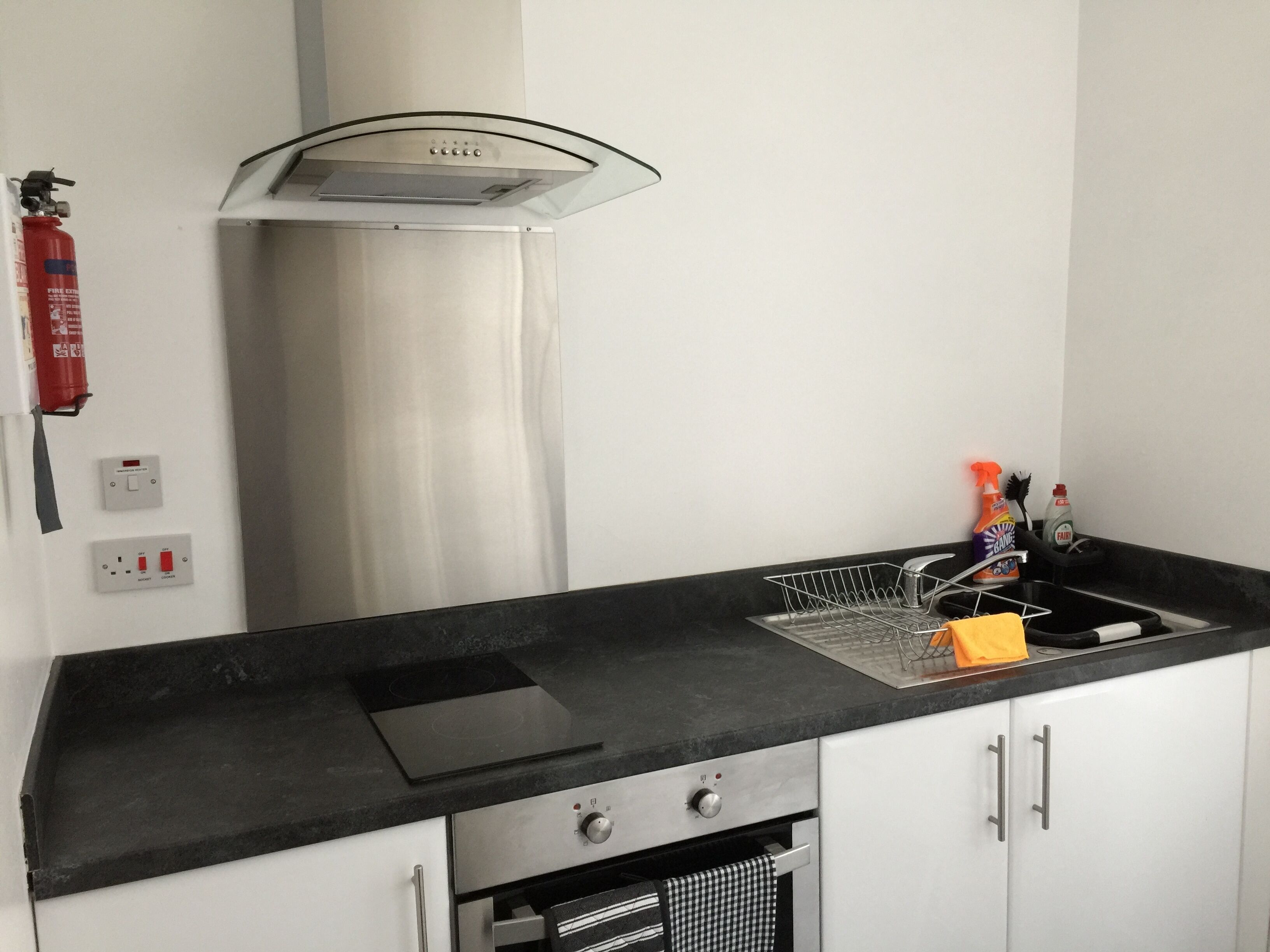 Uma cozinha moderna com bancada preta, eletrodomésticos de aço inoxidável, forno embutido e coifa.