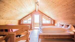 A cozy wooden cabin bedroom with a sloped ceiling, a large bed, and a window providing natural light. - Chalets Trafögl (Val Muestair)