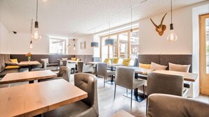 A modern restaurant with wooden tables and chairs, large windows, and decorative light fixtures. - Chalets Trafögl (Val Muestair)