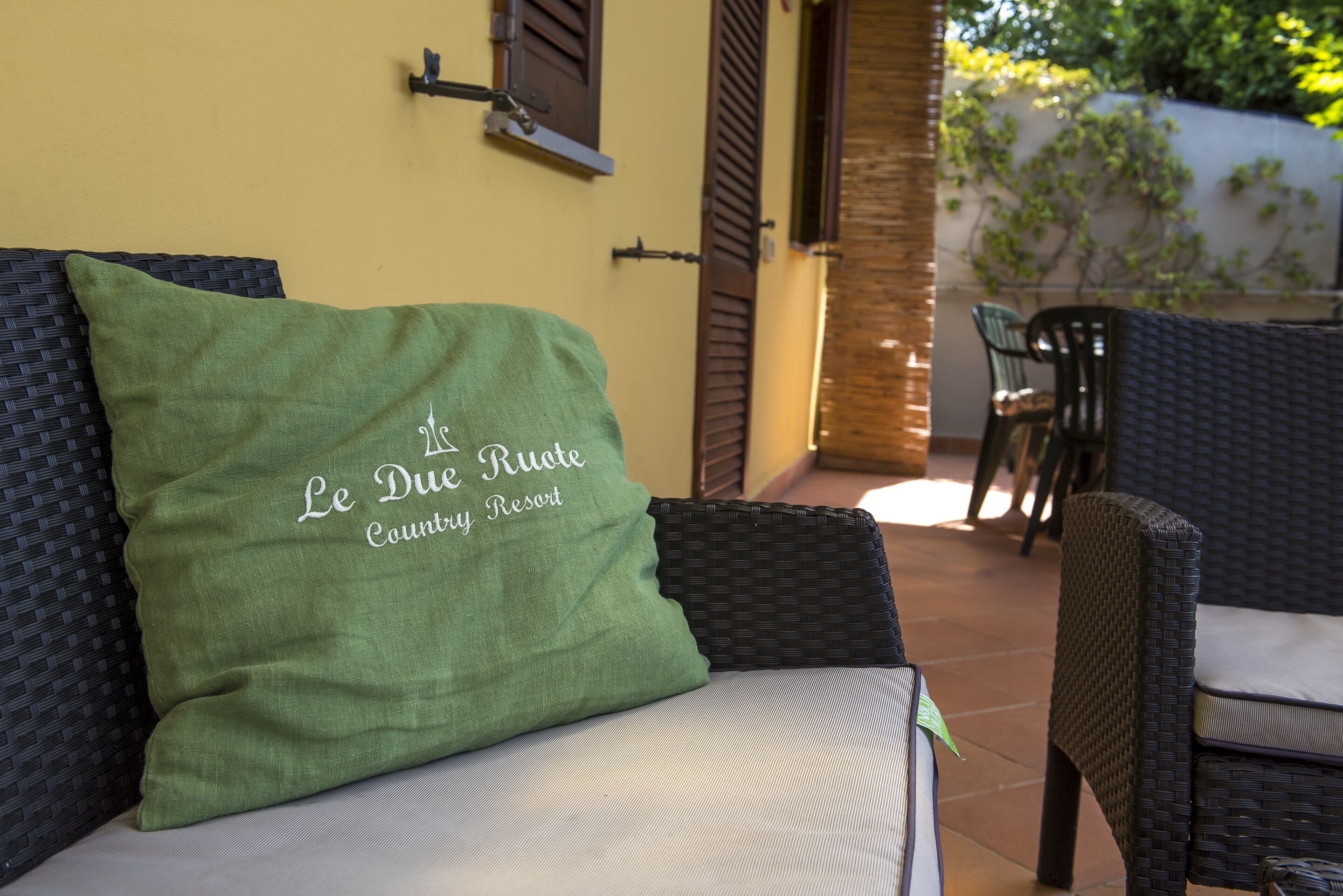 A wicker chair with a green cushion, a wicker sofa, and a wall with a window and shutter.