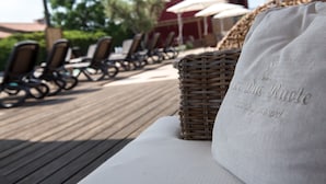 A row of lounge chairs on a wooden deck with a wicker chair and a cushion with embroidered text. - Country Resort Le Due Ruote (Grosseto)