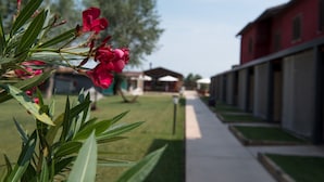 A pathway leading to a building with a red facade, surrounded by greenery and a clear sky. - Country Resort Le Due Ruote (Grosseto)