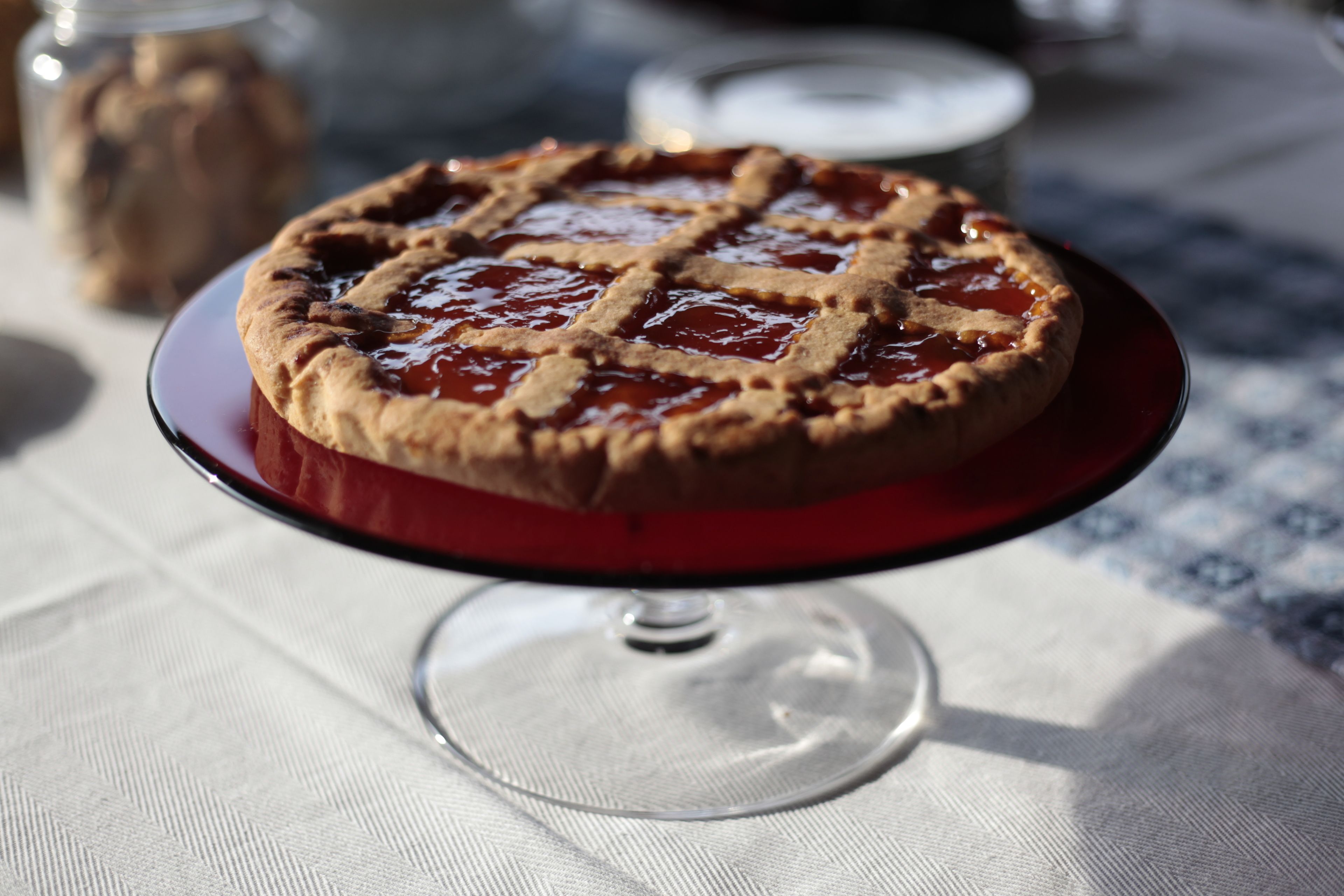 A pie on a glass plate with a lattice crust, placed on a table with a white cloth.