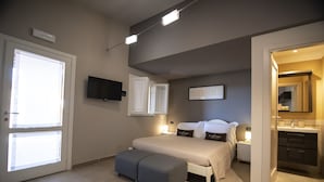 A bedroom with a bed, bedside tables, a TV, and a bathroom visible through an open door. - Country Resort Le Due Ruote (Grosseto)