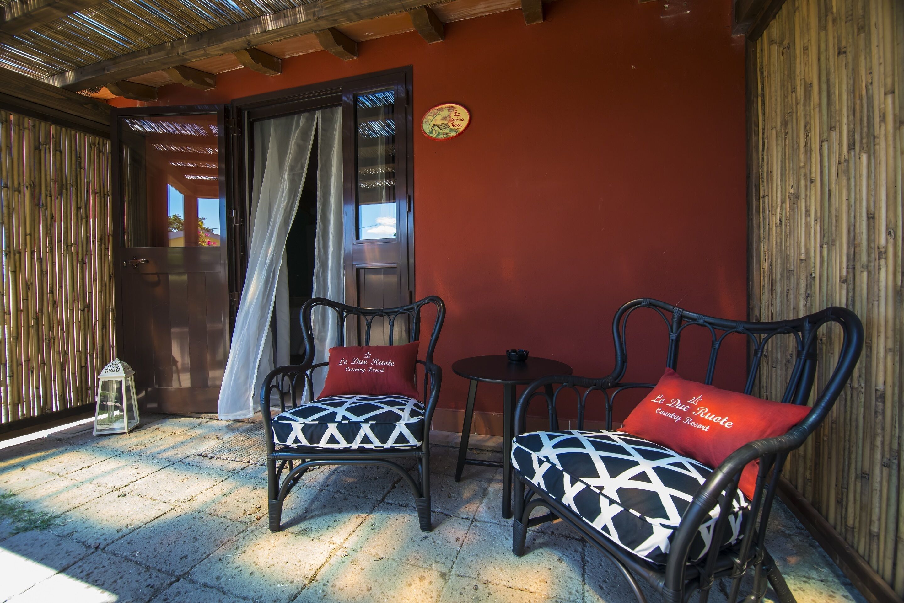 Un patio techado con dos sillas de mimbre, una mesita y una valla de bambú.