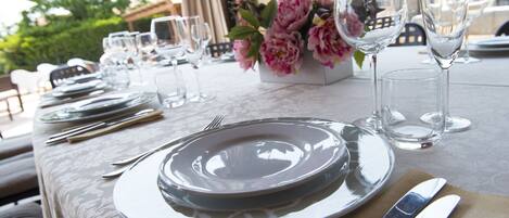 Una mesa lista para comer, con platos, cubiertos y vasos, y un florero con flores.