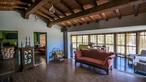 A spacious living room with a wooden ceiling, a red sofa, and a large window with curtains. - Country Resort Le Due Ruote (Grosseto)