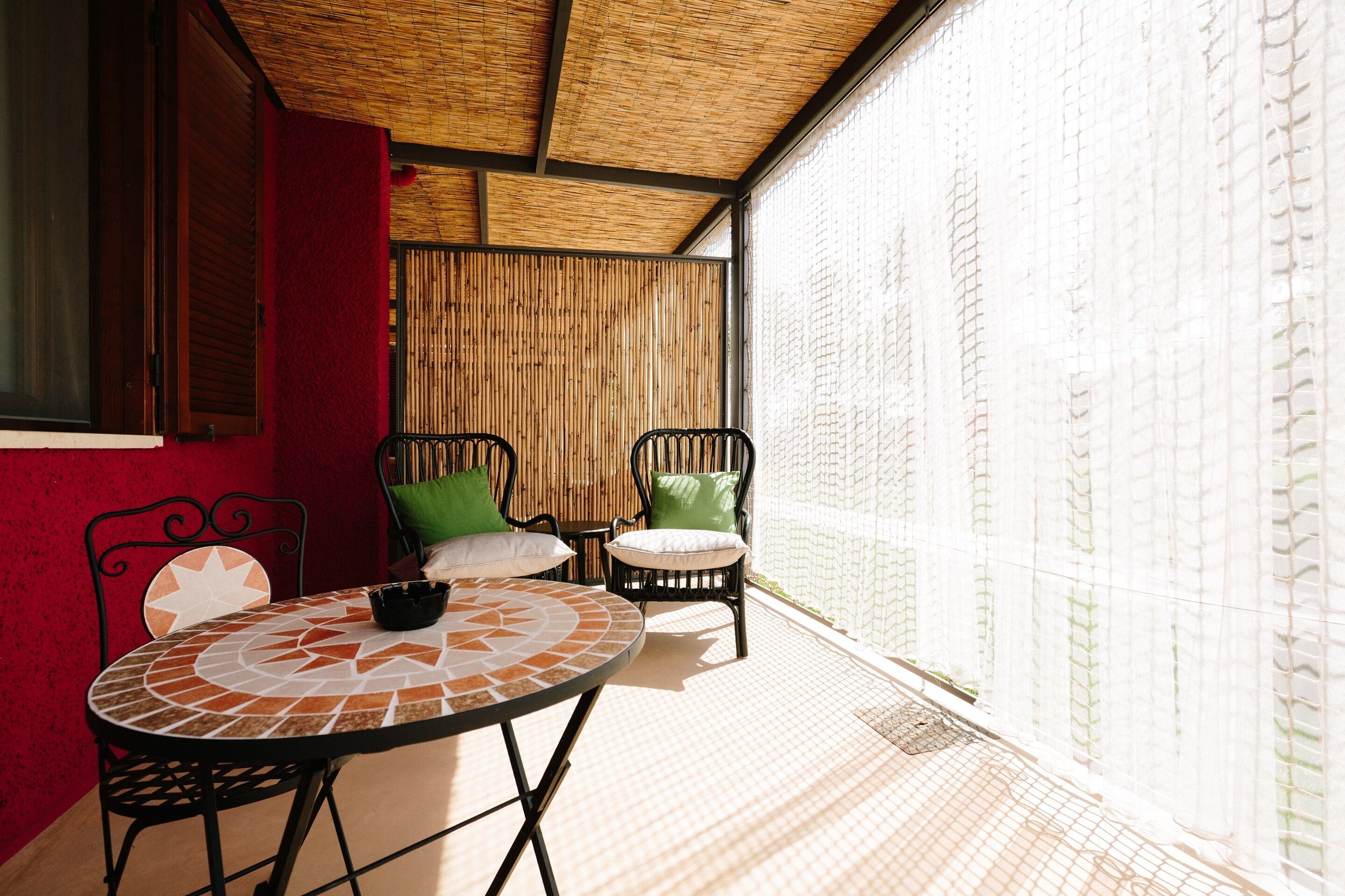Un patio techado con una mesa redonda y dos sillas, una pared roja y una pared de bambú.