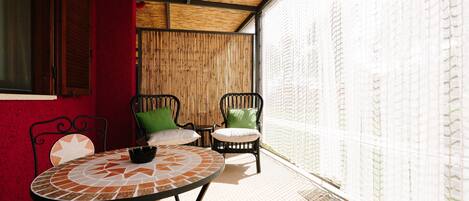 Un patio techado con una mesa redonda y dos sillas, una pared roja y una pared de bambú.