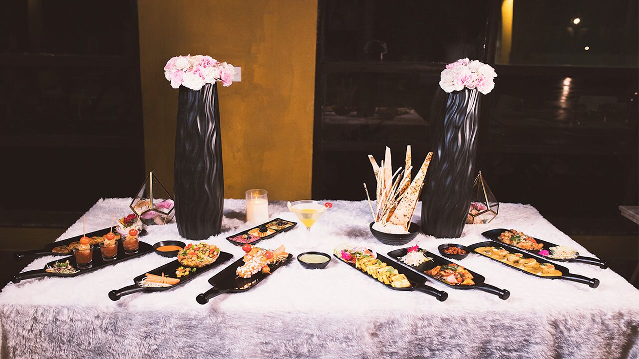 A table set with various dishes and drinks, flanked by tall vases with flowers.