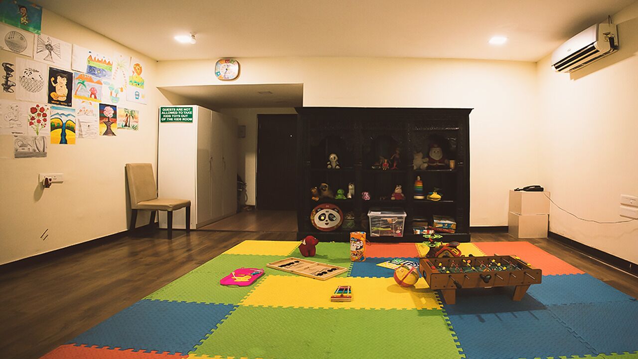 Una habitación con un tapete de juegos de colores, una mesa de futbolín y juguetes infantiles. Hay una silla y una estantería con diversos objetos.