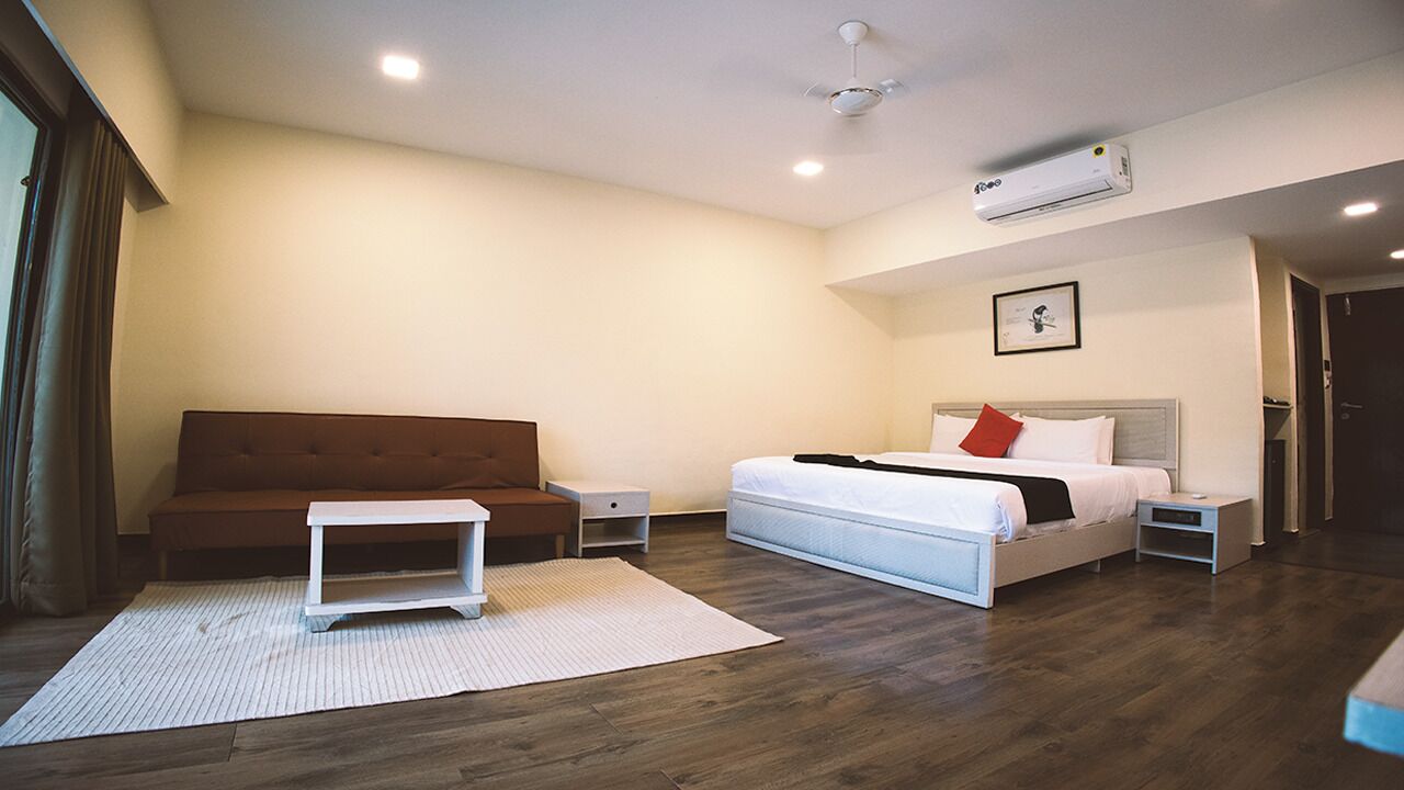 A hotel room with a bed, a small bedside table, a nightstand, a sofa, and a white rug.