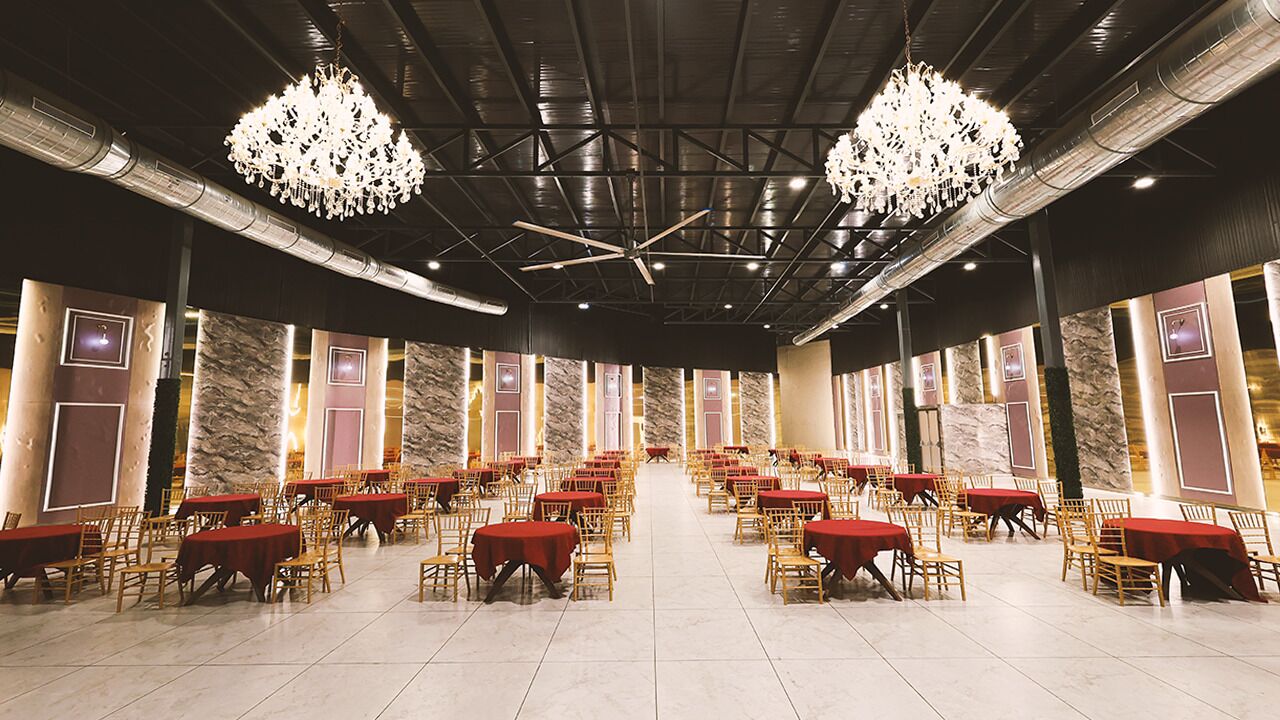 A banquet hall with rows of tables and chairs, large chandeliers, and a high ceiling with exposed beams.