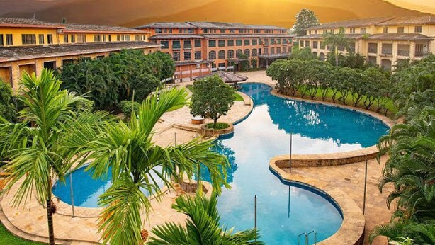 Ett semesterhotell med ett stort poolområde omgivet av palmer och med en bergskedja som bakgrund.