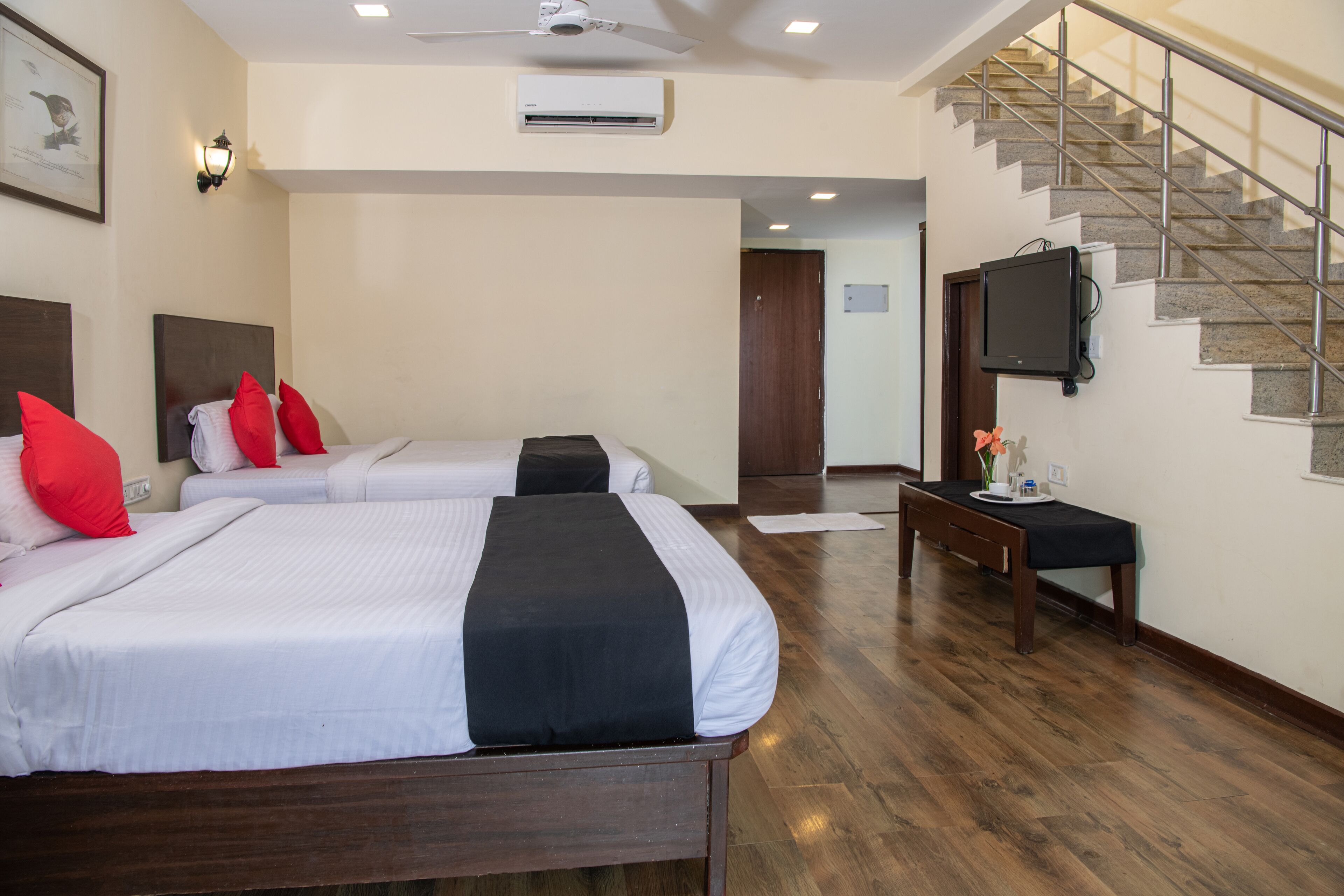 A hotel room with two beds, a TV, a desk, and a staircase.