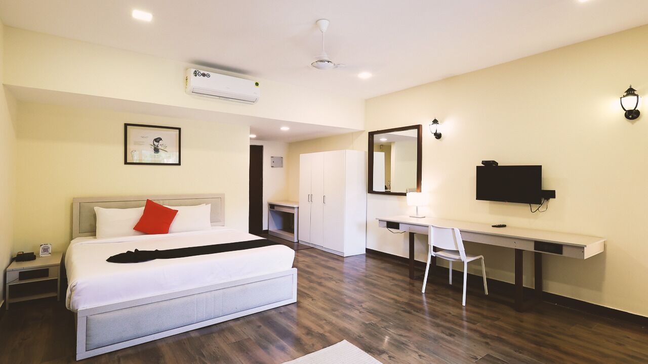 A modern hotel room with a bed, desk, and wardrobe.