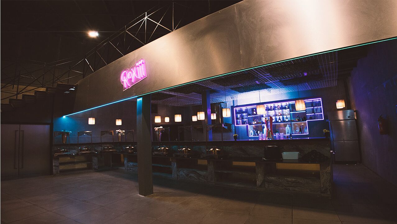 A bar area with a neon sign, seating, and a counter with various items.