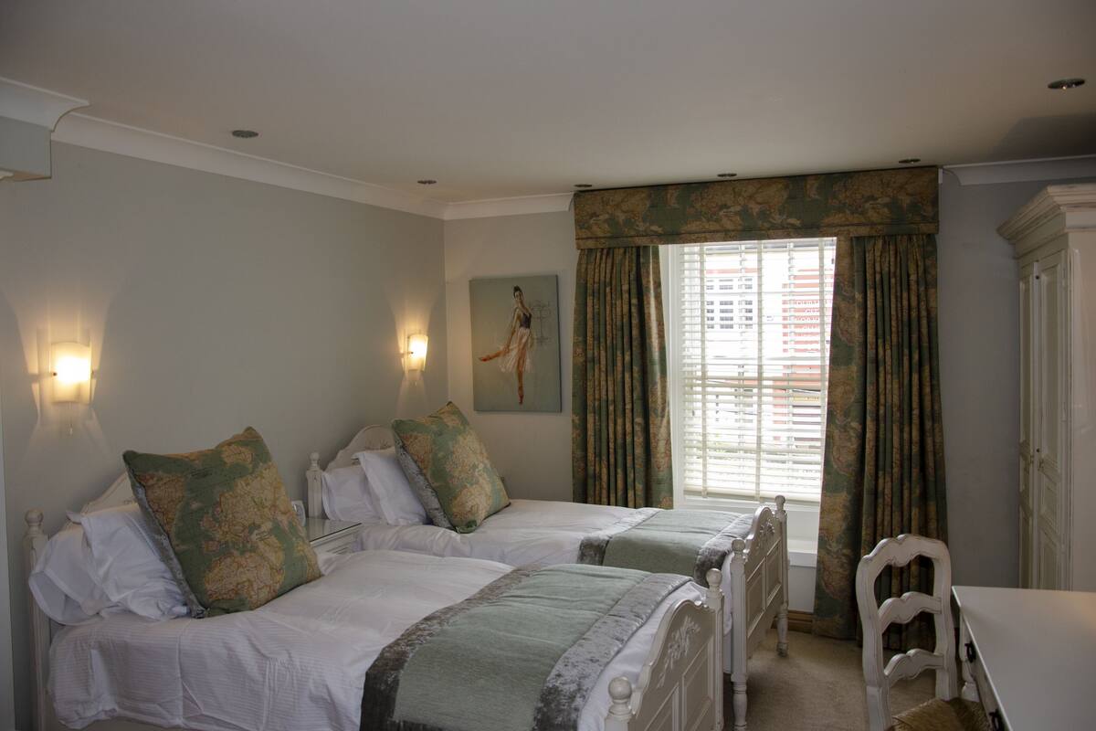 A bedroom with two beds, a chair, and a window with curtains.