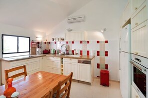 A modern kitchen with white cabinetry, a wooden dining table, and a red trash bin. - MAMAD - Charming Sunny Haven with Balcony by Sea N Rent (Tel Aviv)
