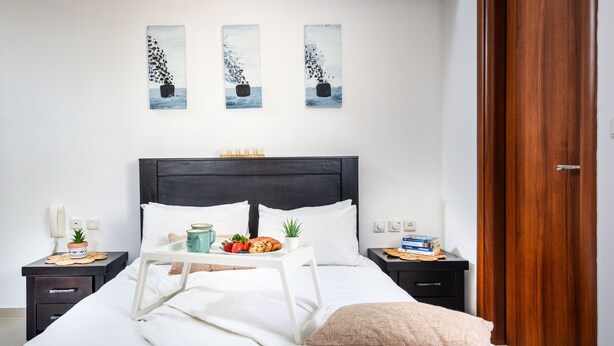 A neatly made bed with white linens, a bedside table with a tray of breakfast items, and a wooden door.