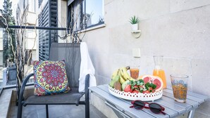 A balcony with a chair, a table with fruit, a glass of juice, and a potted plant.