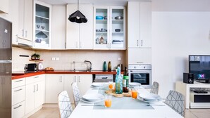 A modern kitchen with white cabinets, a dining table set with plates and glasses, and a TV on the right.