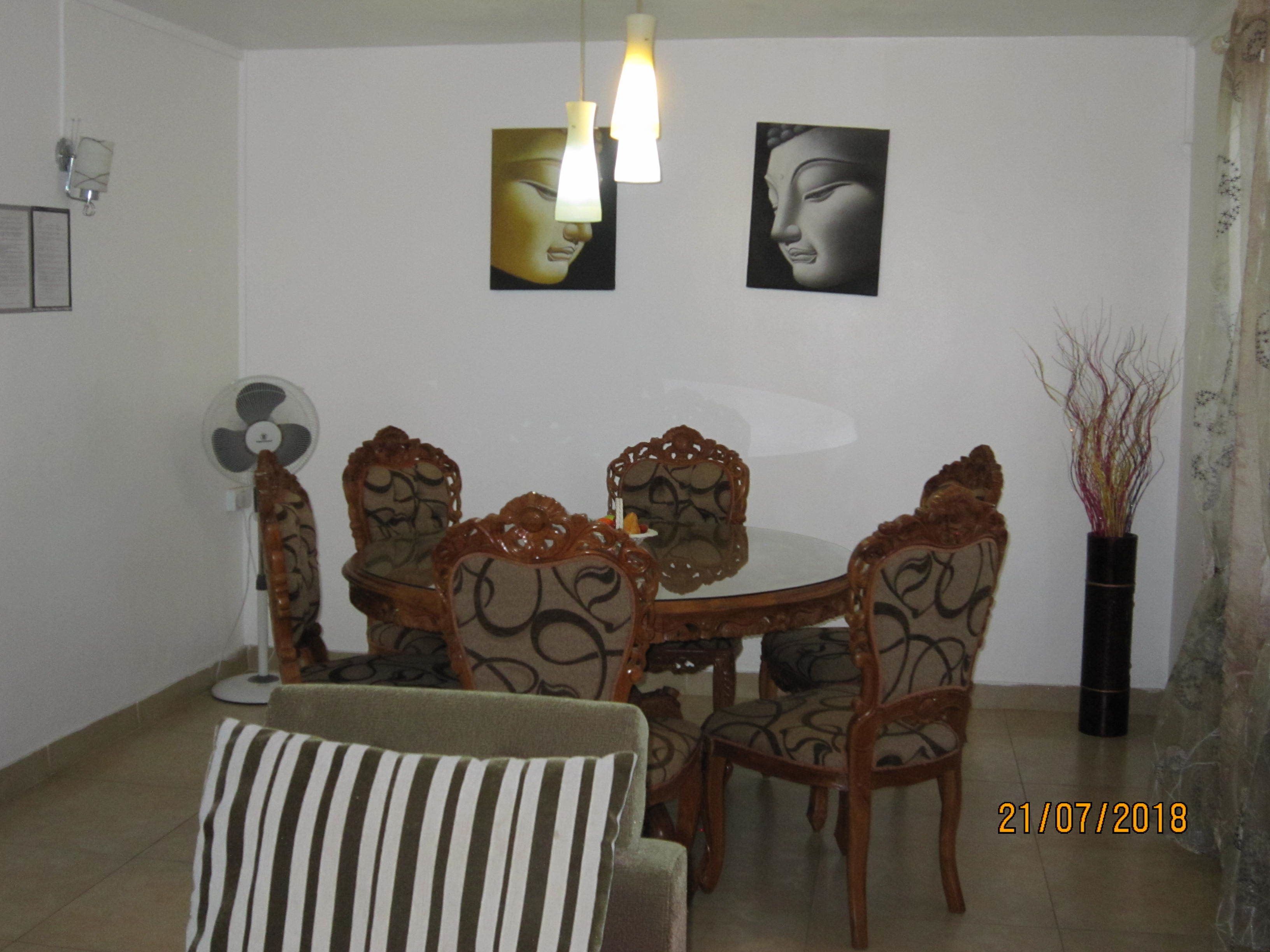 Un comedor con una mesa redonda, seis sillas con diseños elaborados, dos lámparas de pared y dos obras de arte enmarcadas.