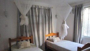 Two single beds with wooden headboards, a window with curtains, and a mosquito net over the beds. - Jolie Villa Santa (Pointe Aux Piments)