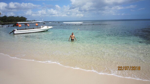 A beach with clear shallow waters, a boat, and a person standing in the water. - Jolie Villa Santa (Pointe Aux Piments)