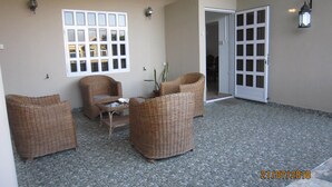 A covered outdoor seating area with wicker furniture, a tiled floor, and a door leading to an interior space. - Jolie Villa Santa (Pointe Aux Piments)