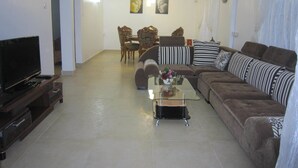 A living room with a sofa, TV, coffee table, and dining area with chairs and a table. - Jolie Villa Santa (Pointe Aux Piments)