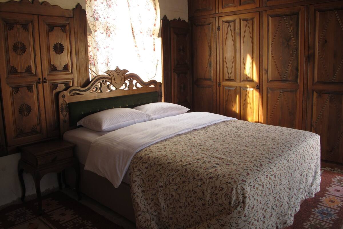 Una camera da letto con una testiera in legno, un letto con lenzuola bianche, un comodino e una coperta a motivi.